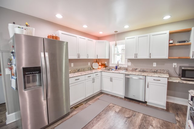 kitchen with light stone countertops, stainless steel appliances, sink, decorative light fixtures, and white cabinetry