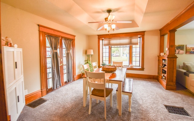 carpeted dining space featuring a raised ceiling and ceiling fan