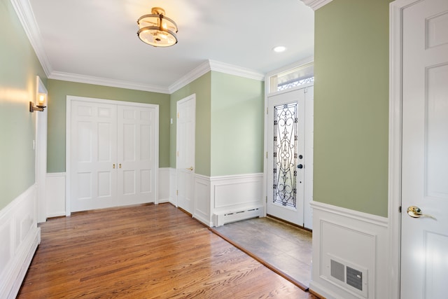 entryway with baseboard heating, hardwood / wood-style flooring, and crown molding