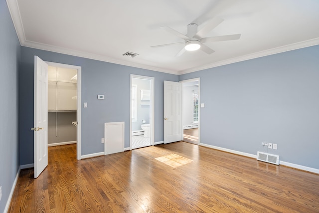 unfurnished bedroom with hardwood / wood-style flooring, ornamental molding, ceiling fan, a closet, and a walk in closet