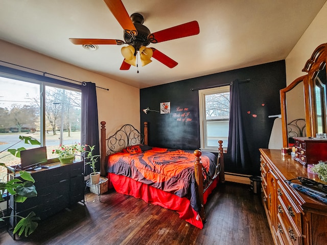 bedroom featuring a baseboard heating unit, dark hardwood / wood-style flooring, multiple windows, and ceiling fan