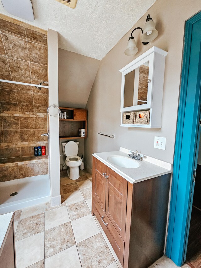 bathroom with tiled shower, vanity, a textured ceiling, vaulted ceiling, and toilet