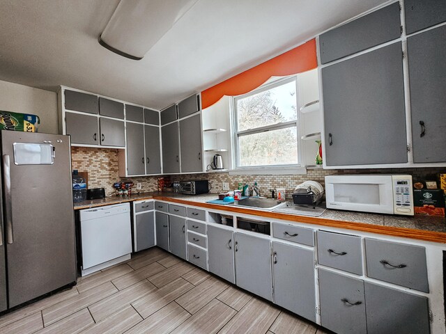 kitchen featuring white appliances, sink, tasteful backsplash, and gray cabinets