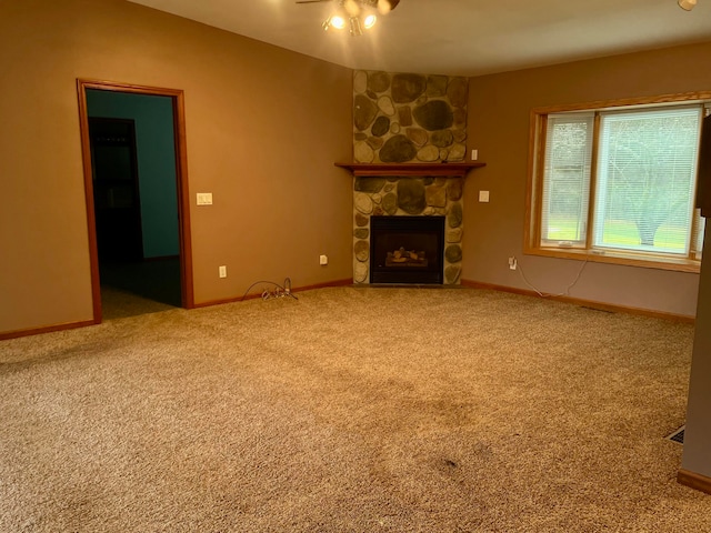 unfurnished living room with carpet flooring, ceiling fan, and a stone fireplace