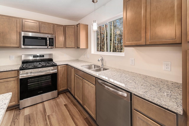 kitchen with light stone countertops, stainless steel appliances, sink, pendant lighting, and light hardwood / wood-style floors