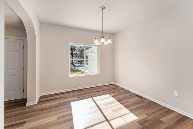 unfurnished dining area featuring wood-type flooring and an inviting chandelier