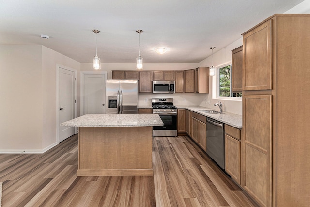 kitchen with sink, hanging light fixtures, a kitchen island, wood-type flooring, and stainless steel appliances