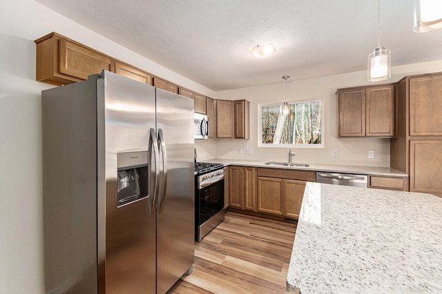 kitchen featuring sink, light hardwood / wood-style floors, decorative light fixtures, and appliances with stainless steel finishes