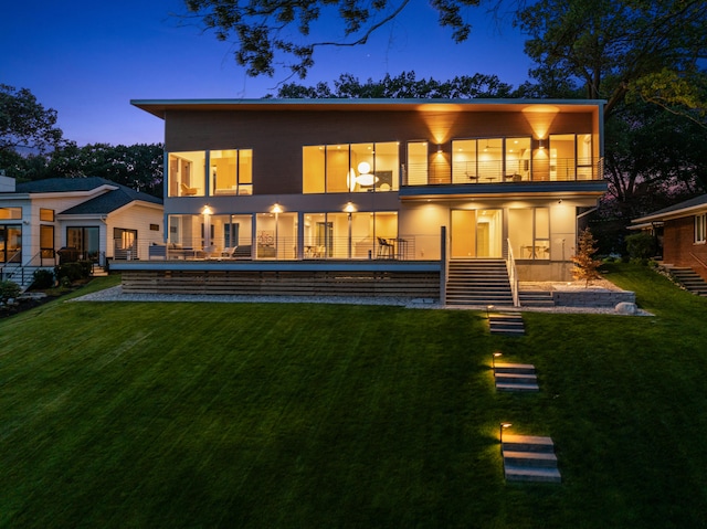 back house at dusk featuring a balcony and a yard