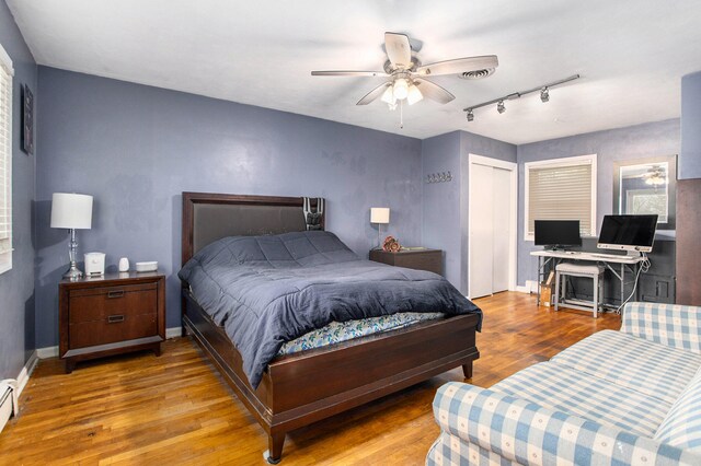 bedroom featuring hardwood / wood-style floors, ceiling fan, a closet, and a baseboard heating unit