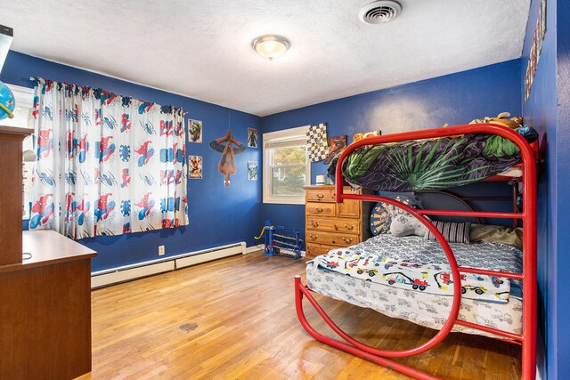 bedroom with a textured ceiling, a baseboard radiator, and hardwood / wood-style flooring