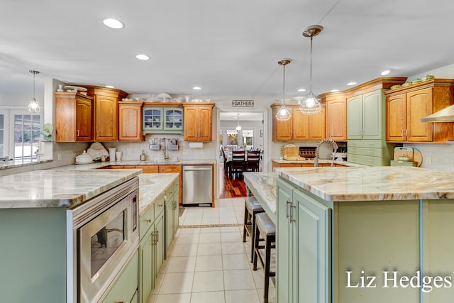 kitchen featuring green cabinetry, stainless steel appliances, hanging light fixtures, and a center island with sink