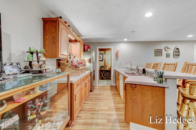 kitchen with stainless steel fridge, white dishwasher, sink, a kitchen breakfast bar, and light hardwood / wood-style flooring