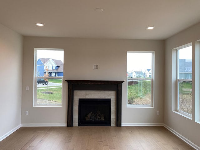 unfurnished living room featuring a healthy amount of sunlight, a tile fireplace, and light wood-type flooring