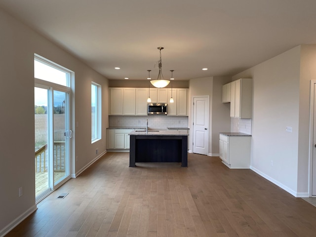 kitchen with hardwood / wood-style flooring, sink, a kitchen island with sink, backsplash, and decorative light fixtures