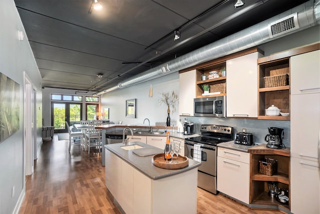 kitchen with stainless steel appliances, white cabinetry, sink, light hardwood / wood-style floors, and a kitchen island with sink