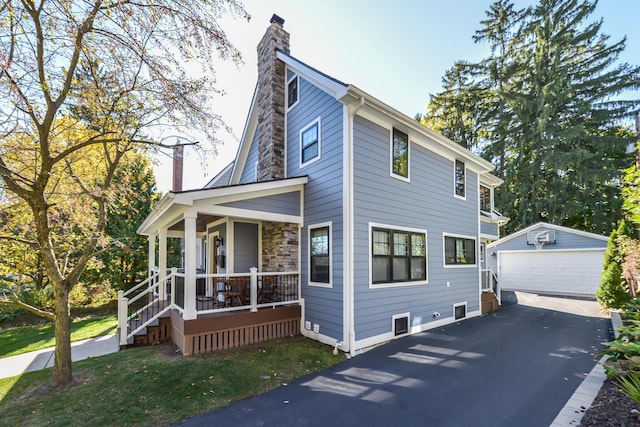 view of front of house with a porch, an outdoor structure, a chimney, and a detached garage