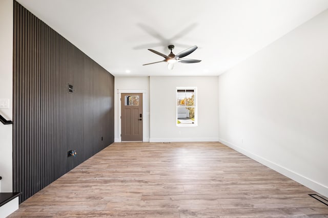 unfurnished room with ceiling fan, light wood-type flooring, and wooden walls