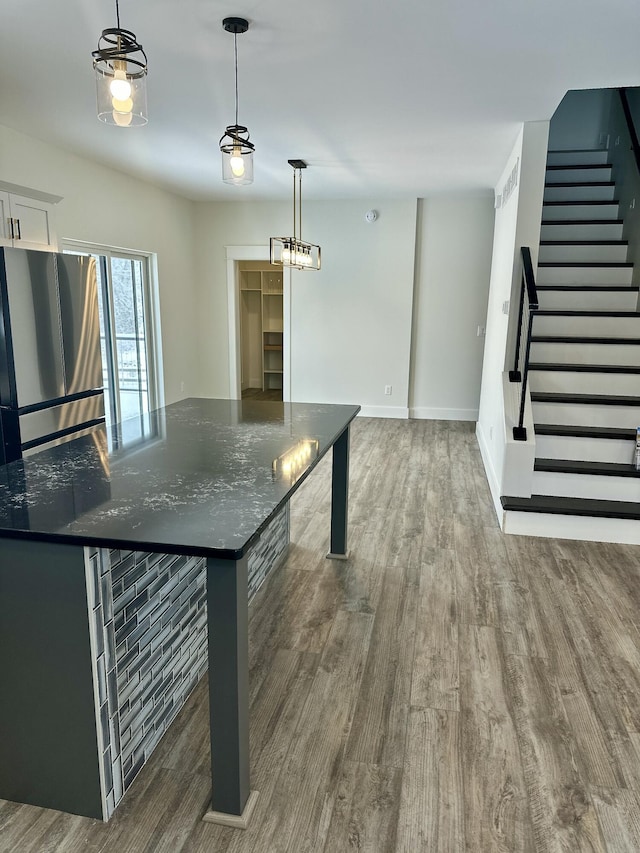 kitchen with hanging light fixtures, dark stone countertops, dark wood-type flooring, and stainless steel refrigerator