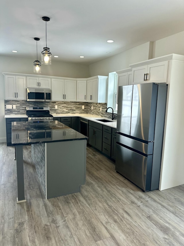 kitchen with stainless steel appliances, sink, decorative light fixtures, light hardwood / wood-style flooring, and white cabinets