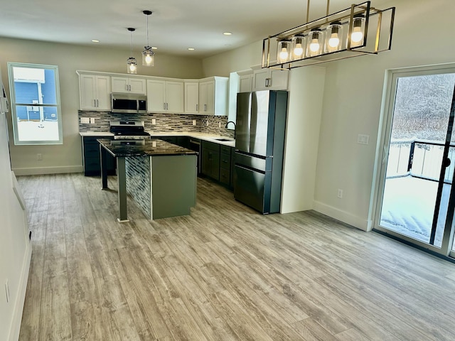 kitchen featuring a wealth of natural light, stainless steel appliances, decorative light fixtures, white cabinets, and a center island