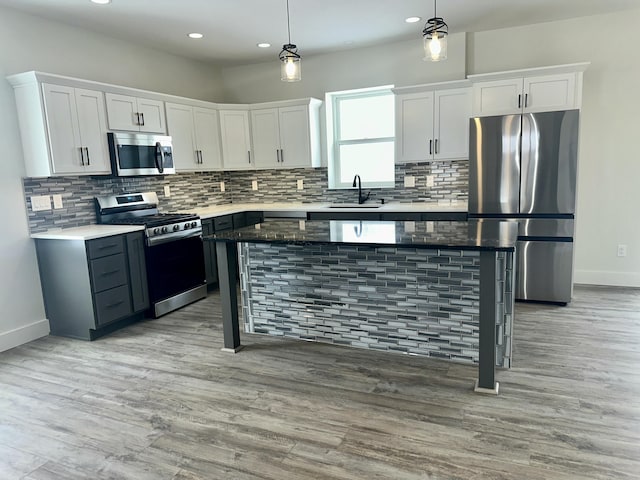 kitchen with appliances with stainless steel finishes, light hardwood / wood-style flooring, a kitchen island, and hanging light fixtures