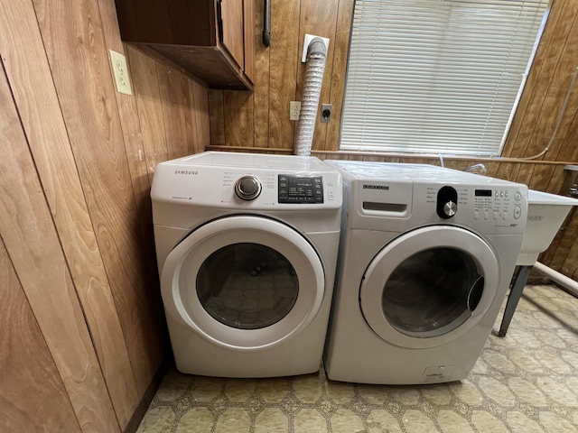 clothes washing area featuring cabinets, wooden walls, and washer and dryer