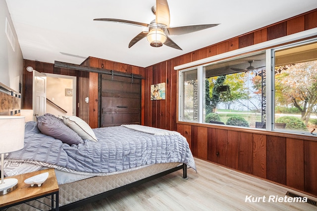 bedroom featuring wood walls, a barn door, ceiling fan, and light hardwood / wood-style flooring