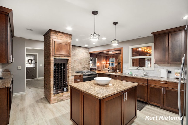 kitchen featuring a kitchen island, light stone countertops, hanging light fixtures, sink, and light hardwood / wood-style floors