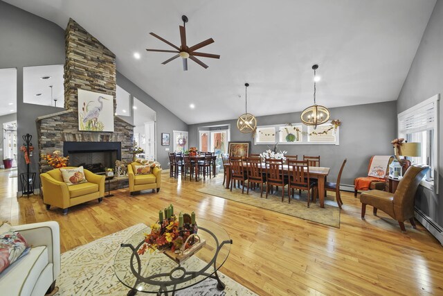 living room with a stone fireplace, a healthy amount of sunlight, ceiling fan with notable chandelier, and light hardwood / wood-style floors