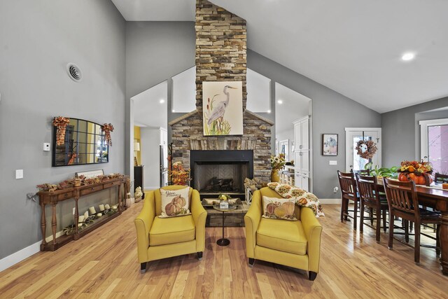 living room with a fireplace, high vaulted ceiling, and light hardwood / wood-style flooring