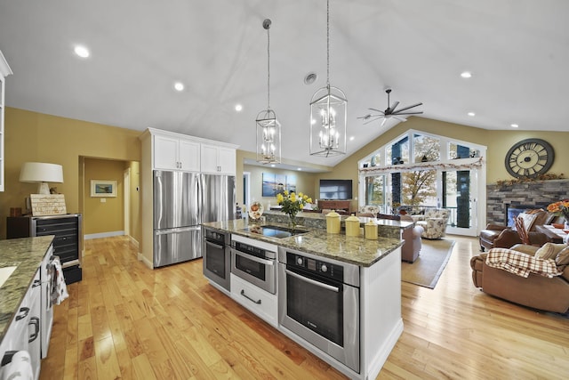 kitchen with appliances with stainless steel finishes, pendant lighting, lofted ceiling, white cabinets, and light wood-type flooring