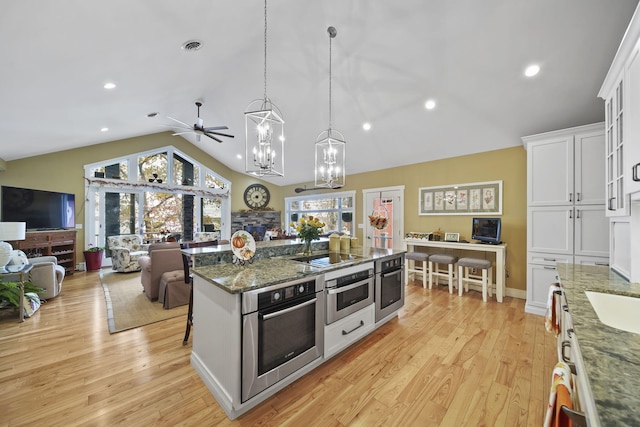 kitchen featuring light hardwood / wood-style flooring, oven, pendant lighting, a kitchen bar, and white cabinets