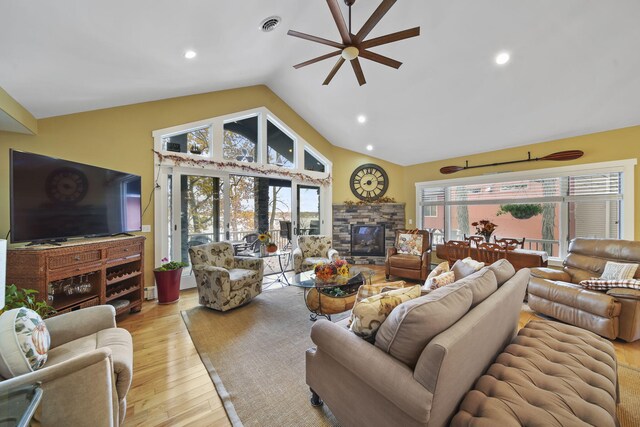 living room with a healthy amount of sunlight, a stone fireplace, light wood-type flooring, and vaulted ceiling