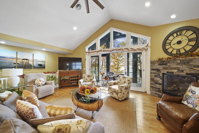 living room featuring a fireplace, light wood-type flooring, vaulted ceiling, and ceiling fan