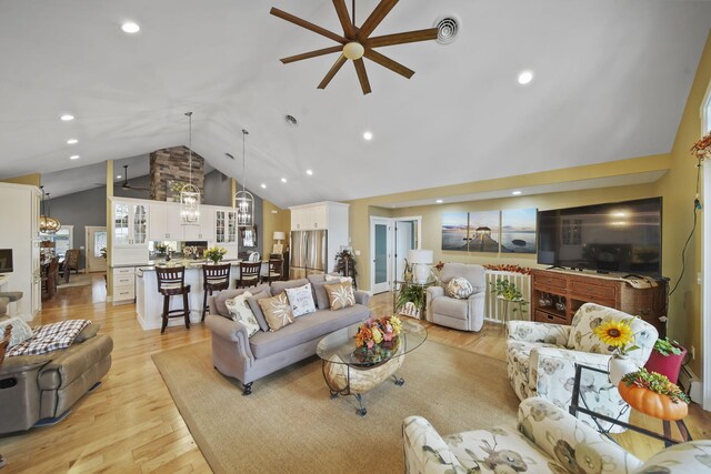 living room with ceiling fan with notable chandelier, light hardwood / wood-style floors, and lofted ceiling