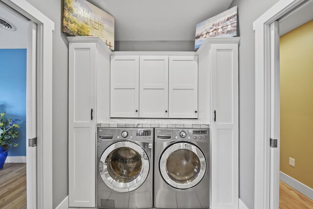 laundry area featuring washer and clothes dryer, cabinets, and light wood-type flooring