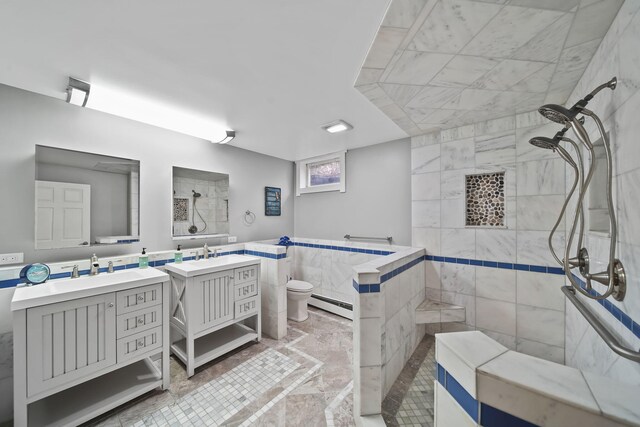 bathroom with a tile shower, a baseboard heating unit, toilet, vanity, and tile walls