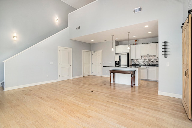 kitchen featuring a high ceiling, hanging light fixtures, a center island, a barn door, and stainless steel fridge