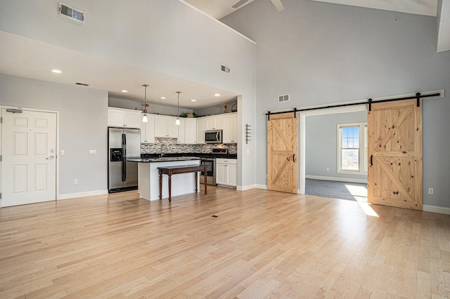 unfurnished living room featuring light hardwood / wood-style flooring, a barn door, a high ceiling, and sink