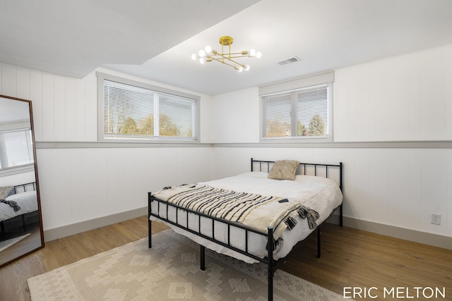 bedroom with wood-type flooring, multiple windows, wooden walls, and an inviting chandelier