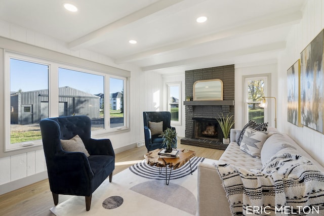 living room featuring a brick fireplace, light hardwood / wood-style floors, and beam ceiling