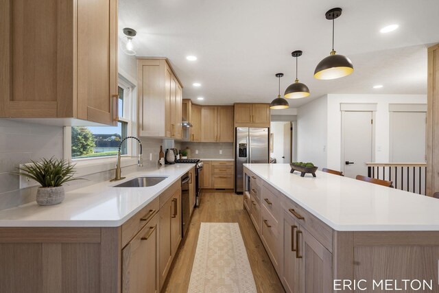 kitchen with sink, stainless steel fridge with ice dispenser, a kitchen island, light hardwood / wood-style flooring, and decorative light fixtures