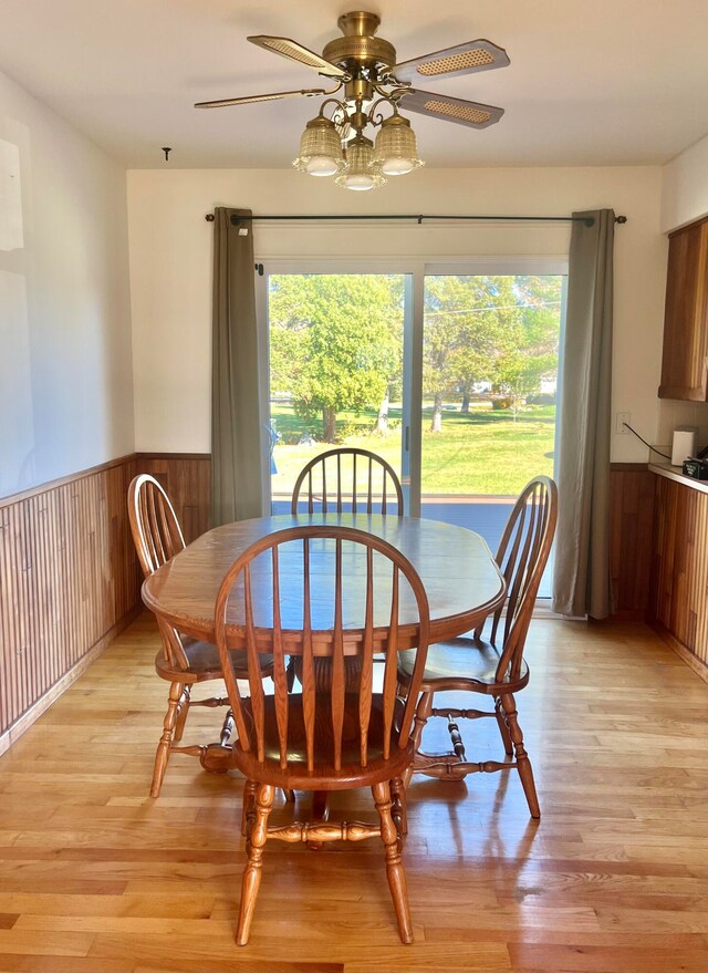 dining area featuring ceiling fan, wood walls, and light wood-type flooring