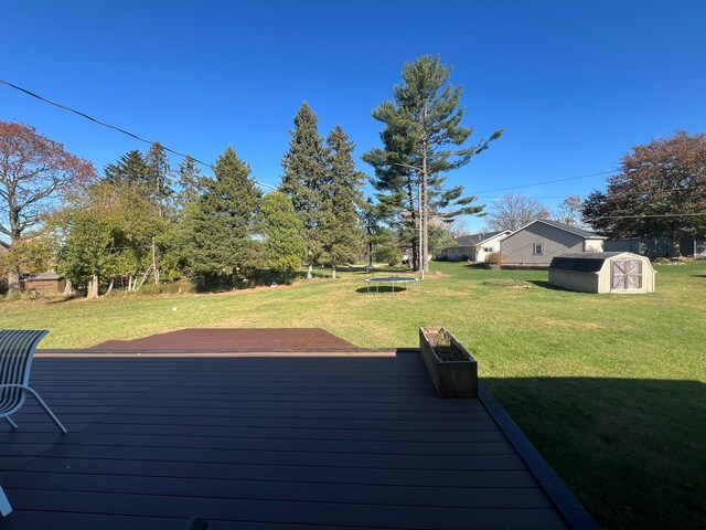 wooden terrace with a trampoline, a shed, and a lawn