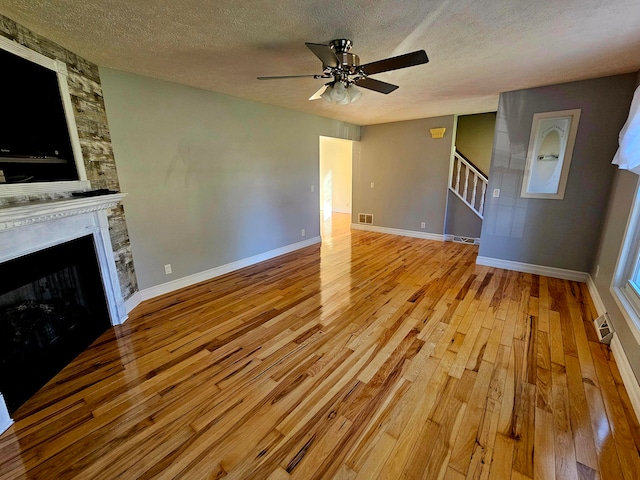 unfurnished living room with light wood-type flooring, a textured ceiling, ceiling fan, and a fireplace