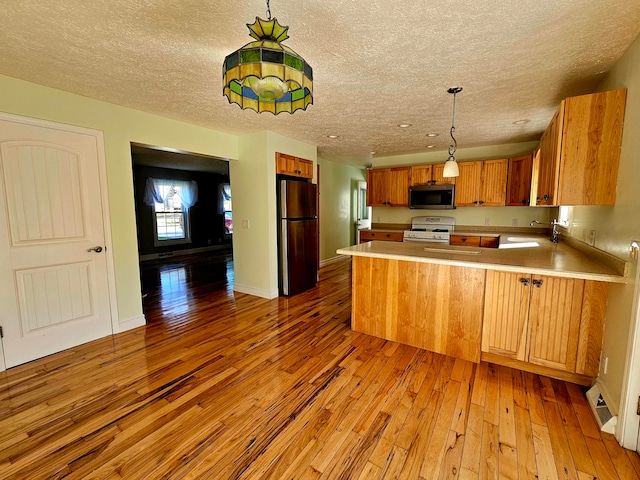 kitchen featuring stainless steel appliances, pendant lighting, sink, kitchen peninsula, and light hardwood / wood-style flooring