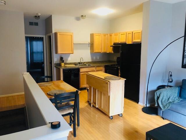 kitchen with light wood-type flooring, light brown cabinets, black appliances, and a center island