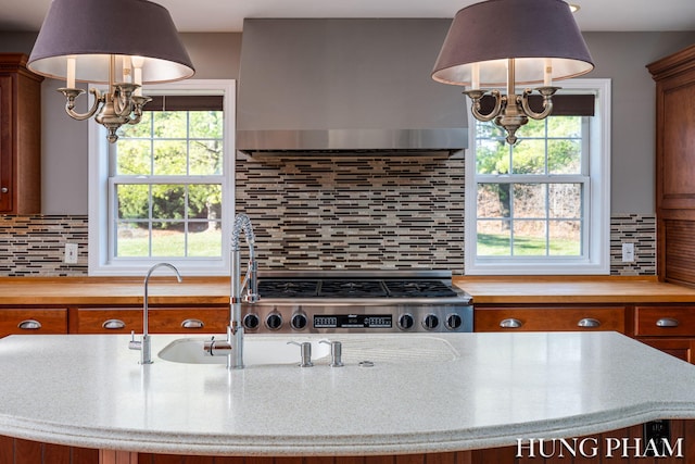 kitchen with a notable chandelier, wall chimney range hood, backsplash, wood counters, and pendant lighting