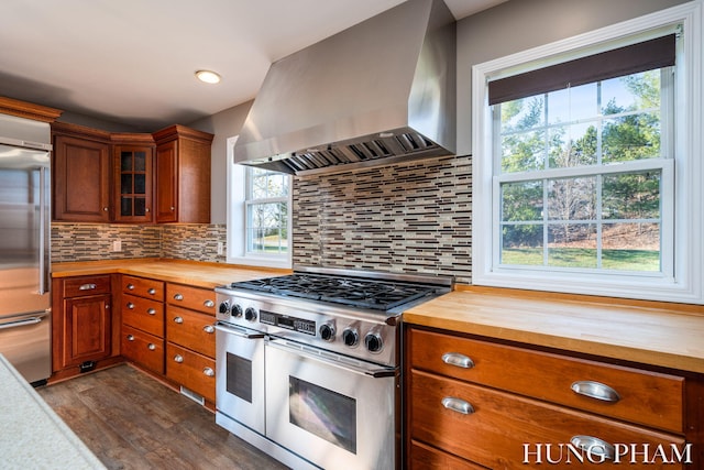 kitchen with wooden counters, dark wood-type flooring, high end appliances, wall chimney exhaust hood, and tasteful backsplash